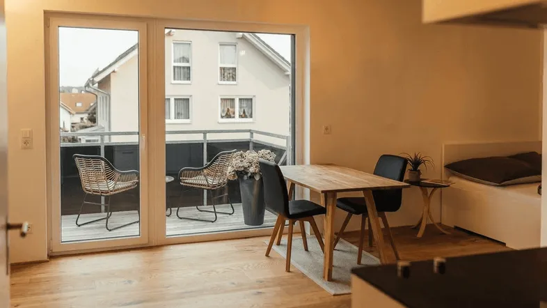 Heller Wohn- und Essbereich mit Holzboden und Zugang zu einem möblierten Balkon.
