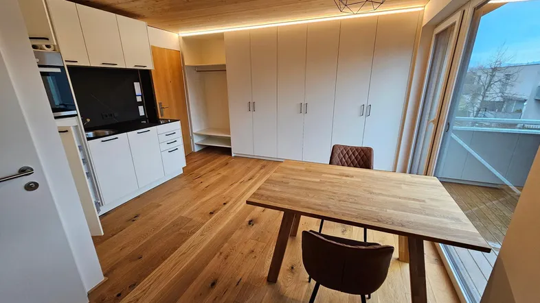 Heller Wohnbereich mit Holzboden, integrierter Küchenzeile und Einbauschränken, mit Zugang zum Balkon.