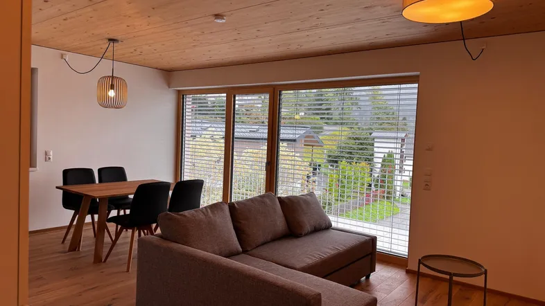 Helles Wohn- und Esszimmer mit Holzboden, bequemer Couch und Zugang zum Balkon.
