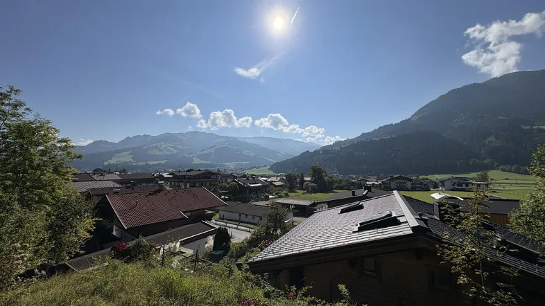 Panoramablick über ein malerisches Dorf im Tal, umgeben von grünen Bergen unter strahlend blauem Himmel.