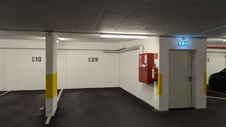 Tiefgaragenstellplatz mit klaren Markierungen, Feuerlöscher und Notausgang in einem funktionalen Bereich.