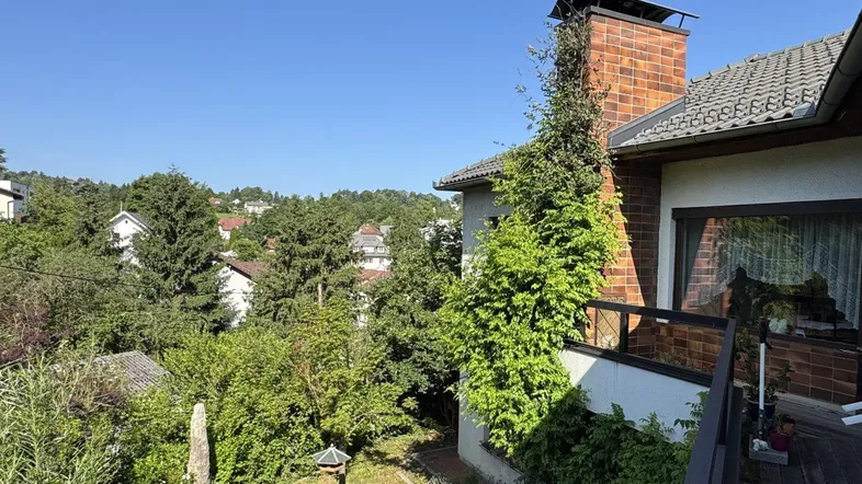 Balkon mit Blick ins Grüne und auf die umliegende Wohngegend unter blauem Himmel.