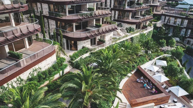 Luftaufnahme von luxuriösen Apartmentgebäuden mit üppiger Vegetation und einer Holzterrasse am Meer.