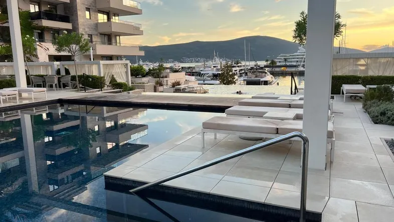 Luxuriöser Poolbereich mit Liegestühlen und Blick auf den Hafen und die Berge bei Sonnenuntergang.