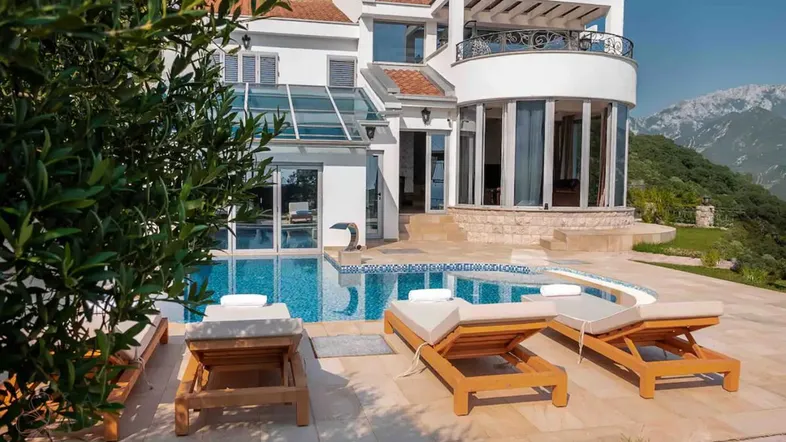 Luxuriöse Villa mit großem Außenpool, Sonnenliegen und Bergblick, umgeben von mediterraner Vegetation.