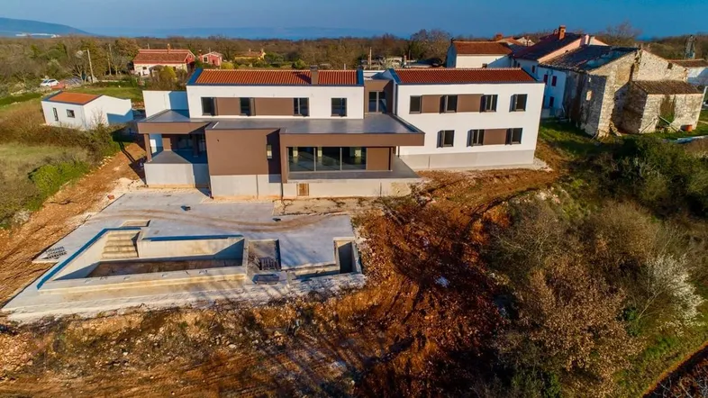 Moderne Villa im Bau mit Rohbau des Pools und Blick auf die umliegende Landschaft.