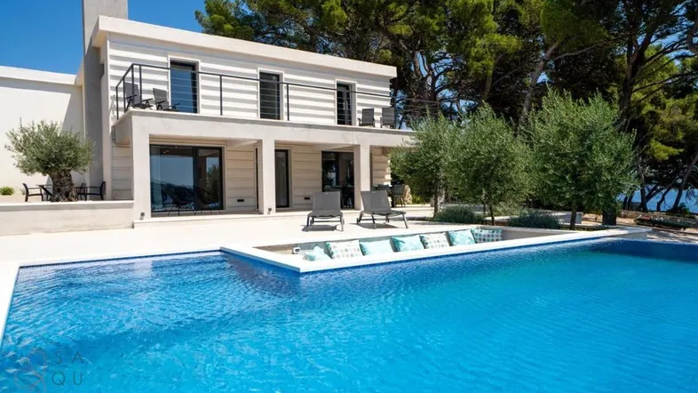 Moderne Villa mit großem Poolbereich und Liegestühlen unter blauem Himmel.