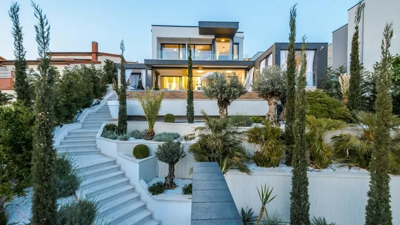 Moderne Villa mit gestuften Gärten, Treppen und mediterraner Bepflanzung bei Sonnenuntergang.