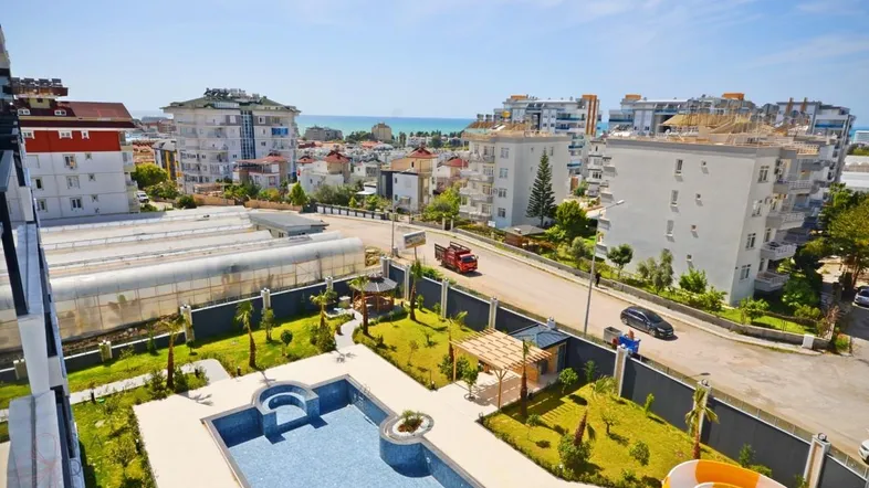 Panoramablick auf die Wohnanlage mit Pool, Garten und Meer im Hintergrund unter blauem Himmel.