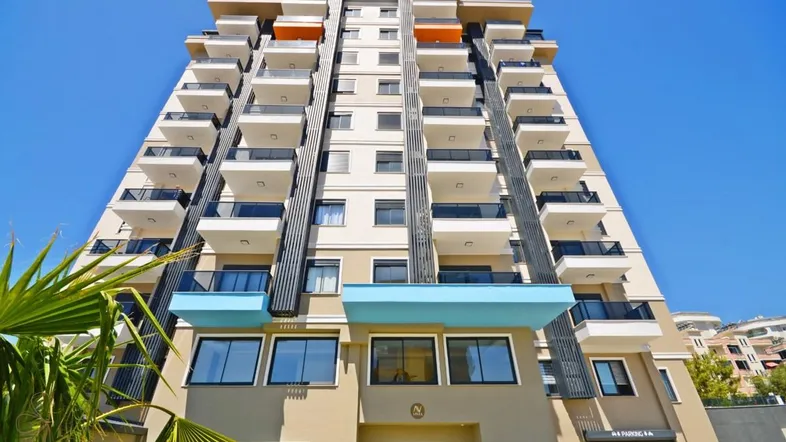 Moderne Wohnanlage mit vielen Balkonen und Glasgeländern unter blauem Himmel.