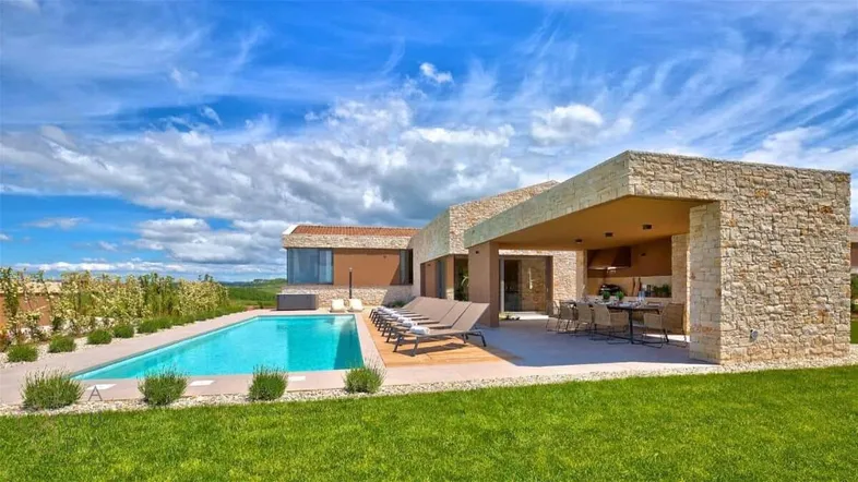 Moderne Villa mit Steinfassade, großem Pool, Sonnenliegen und überdachtem Essbereich im Freien.