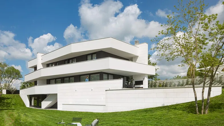 Moderne Villa mit weißer Fassade und weitläufigem Rasenbereich unter blauem Himmel.