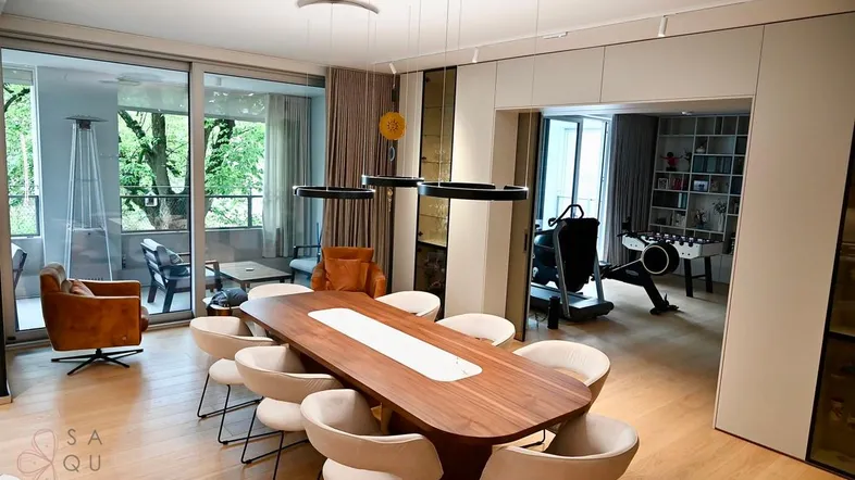 Moderner offener Wohn- und Essbereich mit Zugang zum Balkon und Fitnessbereich.