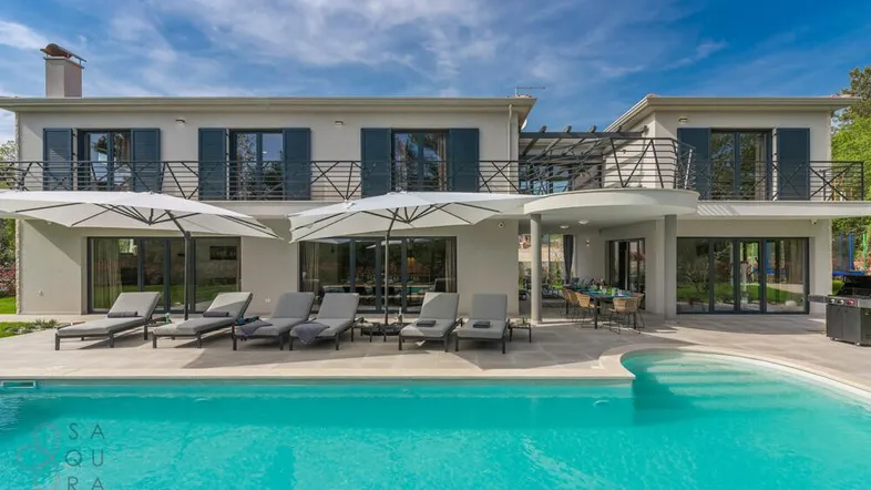 Moderne Villa mit großem Poolbereich, Sonnenliegen und überdachtem Essbereich im Freien.