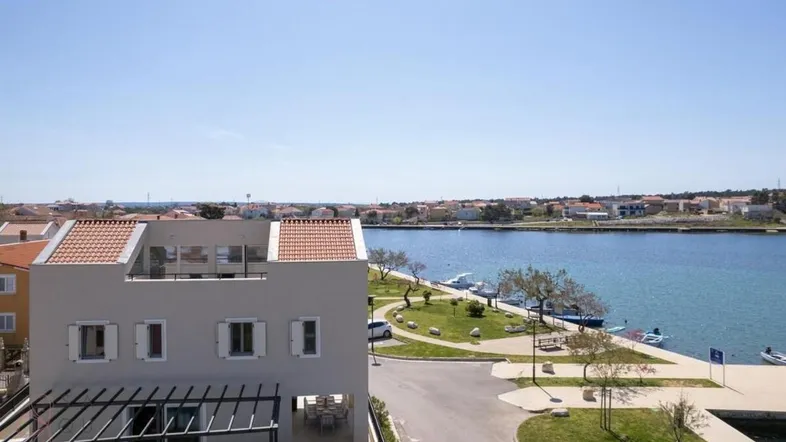 Panoramablick auf das moderne Gebäude mit Terrakottadach und die umliegende Küstenlandschaft mit Wasser.