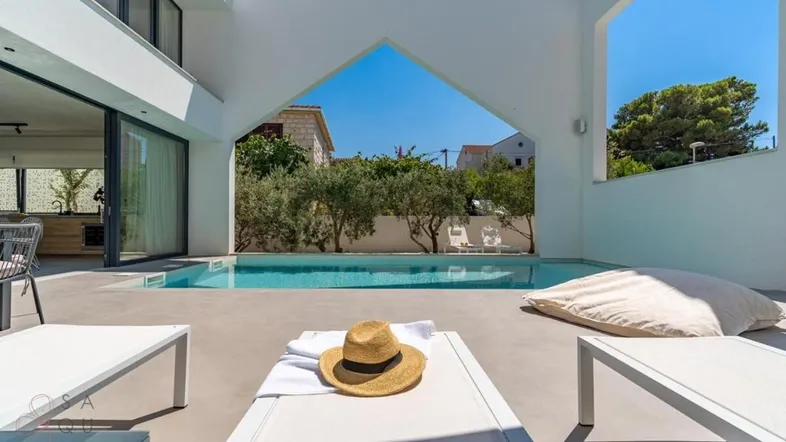 Heller Außenbereich mit Pool, Liegestühlen und Blick auf die Umgebung unter blauem Himmel.