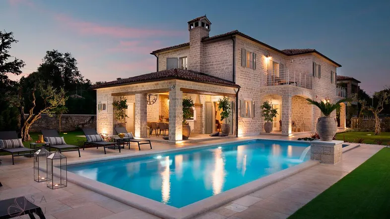 Elegante Villa mit beleuchtetem Pool und überdachter Terrasse bei Sonnenuntergang.