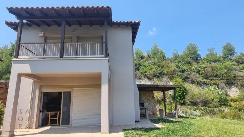 Seitenansicht des Hauses mit Balkon, kleiner Rasenfläche und eingebautem Grillbereich unter blauem Himmel.