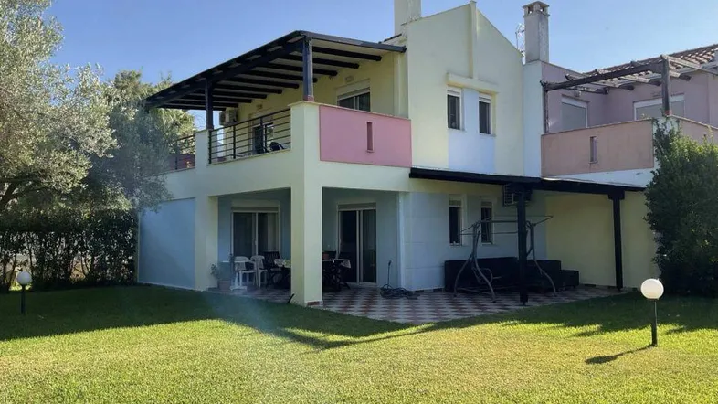 Rückansicht des Hauses mit gepflegtem Rasen, Terrasse und Balkon unter blauem Himmel.