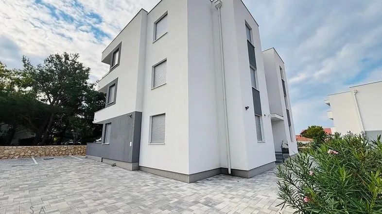 Modernes Mehrfamilienhaus mit weißer und grauer Fassade sowie gepflastertem Parkplatz.