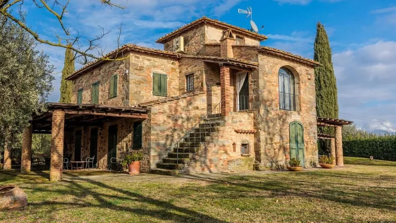 Traditionelles Steinhaus mit grünen Fensterläden und einer Außentreppe, umgeben von einem weitläufigen Garten.