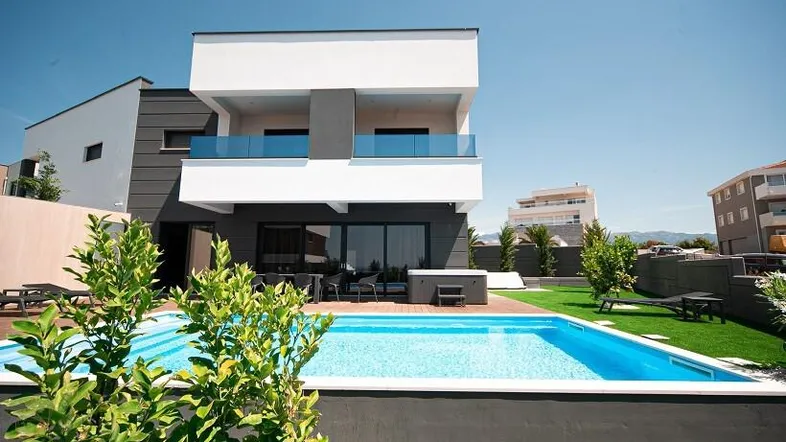 Moderne Villa mit großem Pool und gepflegtem Rasen unter strahlend blauem Himmel.