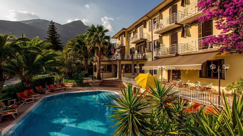 Großzügiger Außenbereich mit Swimmingpool, Palmen und einem Hotelgebäude im Hintergrund.
