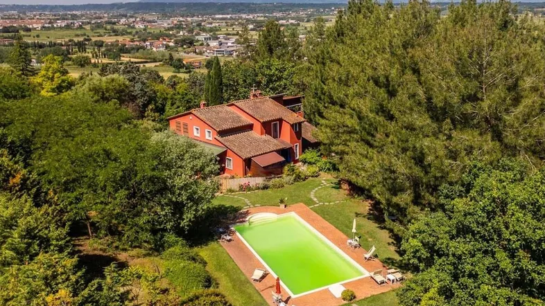Luftaufnahme eines roten Landhauses mit großem Pool, umgeben von üppiger Vegetation und weiter Landschaft.