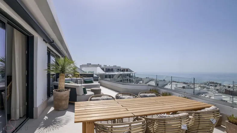 Geräumige Dachterrasse mit Essbereich, Lounge-Möbeln und weitem Meerblick unter strahlend blauem Himmel.