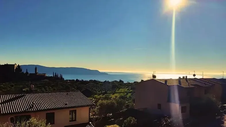 Panoramablick auf das Meer und die umliegende Landschaft mit Häusern und Bergen im Sonnenlicht.
