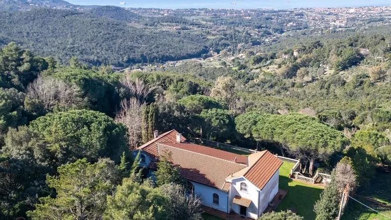 Luftaufnahme eines Hauses in hügeliger Landschaft mit weitem Blick auf das Meer.