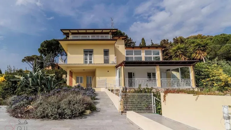 Gelbe Villa mit Auffahrt, mediterraner Bepflanzung und weitem Blick unter blauem Himmel.