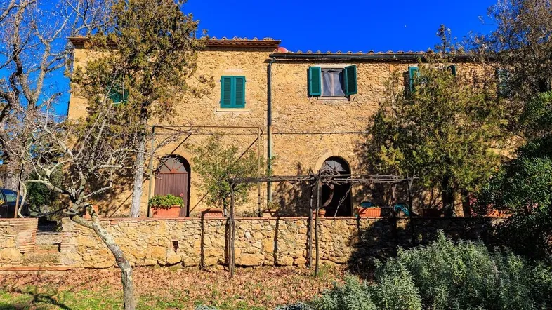 Traditionelles Steinhaus mit grünen Fensterläden und mediterraner Vegetation in sonniger Lage.