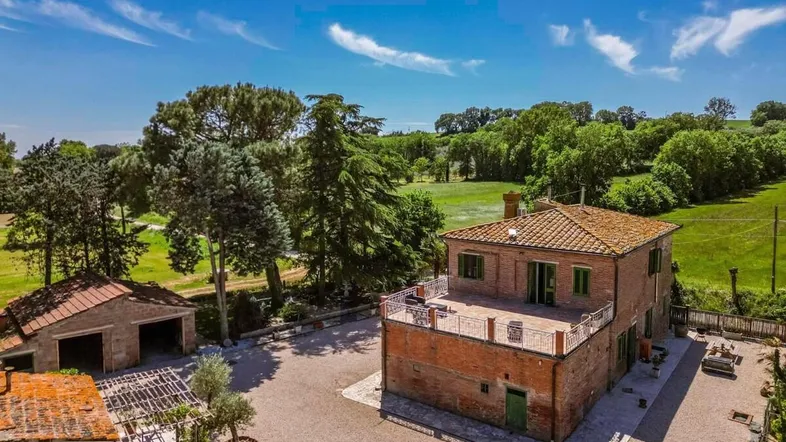Luftaufnahme eines traditionellen Backsteinhauses mit großer Terrasse und weitläufiger grüner Landschaft.