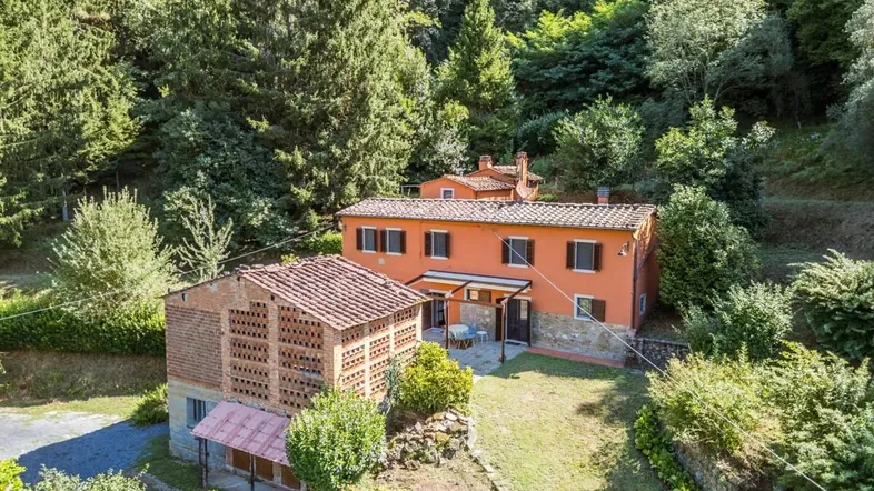 Traditionelles Landhaus mit Terrakottadachziegeln, umgeben von üppiger grüner Vegetation und Bäumen.