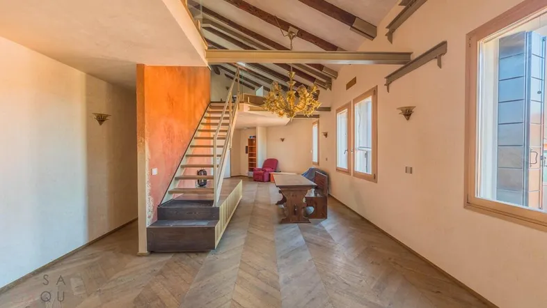 Geräumiger offener Wohn- und Essbereich mit Holzbalken, Fischgrätparkett und einer Treppe zum oberen Bereich.