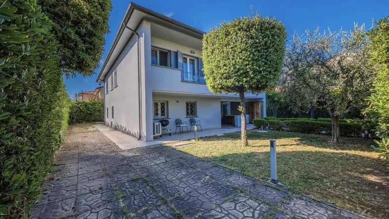Vorderansicht des Hauses mit gepflasterter Auffahrt und gepflegtem Vorgarten unter blauem Himmel.