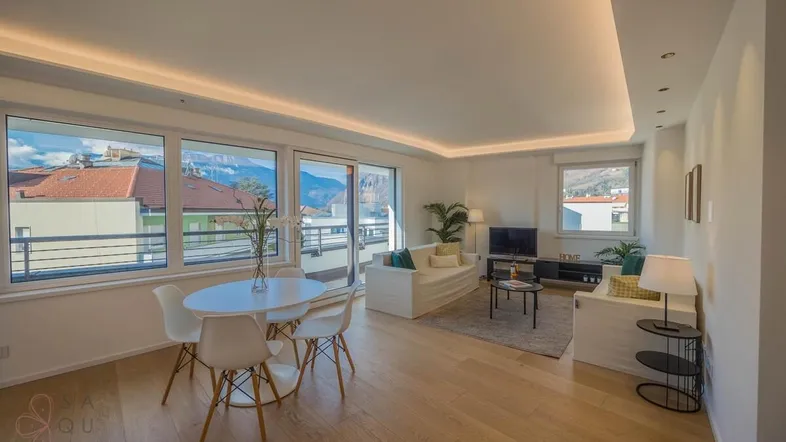 Helles Wohn- und Esszimmer mit Holzboden, modernen Möbeln und Bergblick durch große Fenster.
