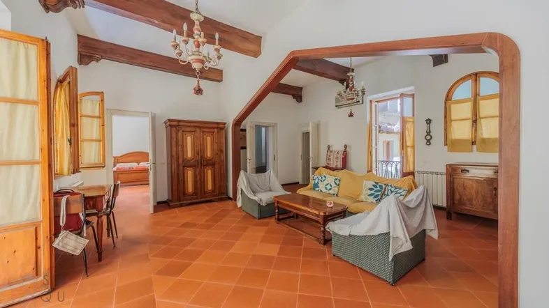 Geräumiges Wohnzimmer mit traditionellen Holzbalken, Terrakottaboden und Zugang zu einem kleinen Balkon.