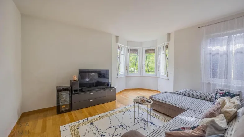 Helles Wohnzimmer mit Parkettboden, Erkerfenstern und gemütlichem Sofa, ideal zum Entspannen.