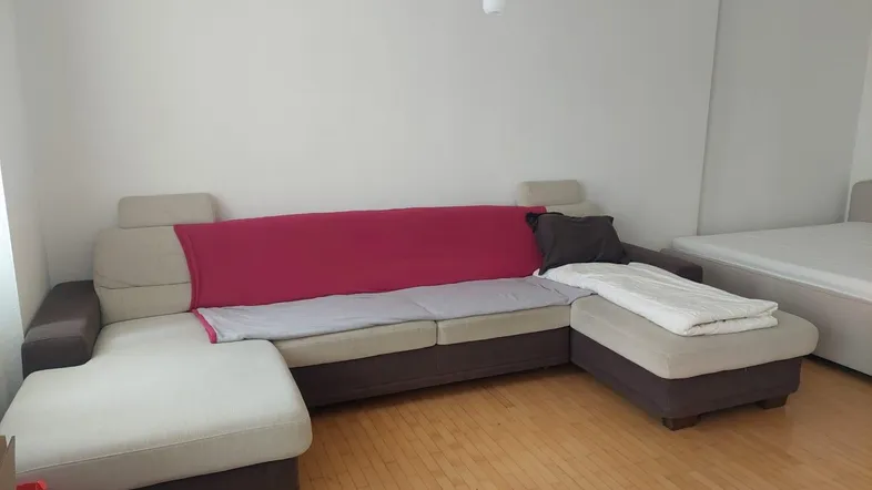 Geräumiger Wohnbereich mit großem Ecksofa und hellem Parkettboden, angrenzend an einen Schlafbereich.