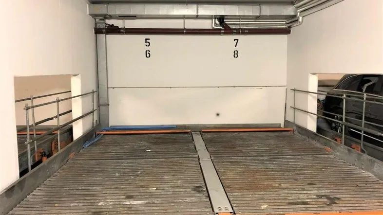 Tiefgaragenstellplatz mit Doppelparker-System für zwei Fahrzeuge und sichtbaren Installationen.