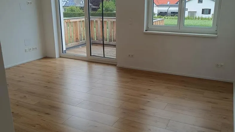 Helles Zimmer mit Holzboden, großen Fenstern und Zugang zu einem Balkon mit Blick auf die Nachbarschaft.
