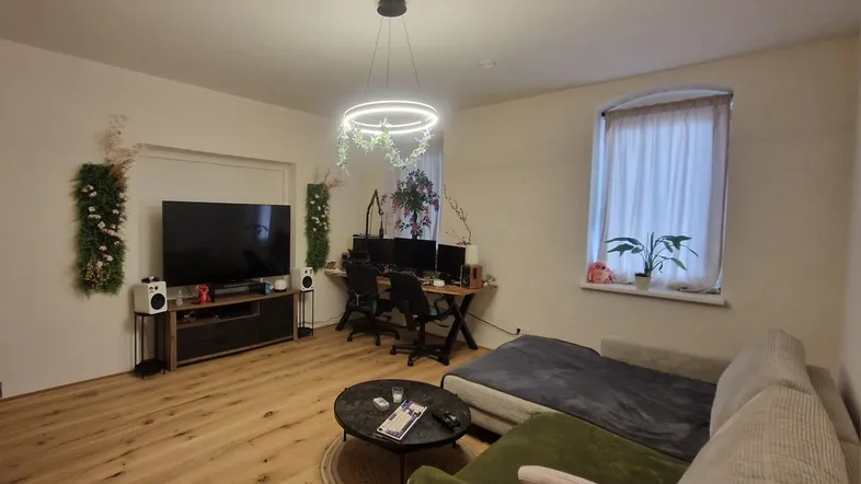 Geräumiges Wohnzimmer mit Holzboden, bequemer Couch, Fernseher und integriertem Arbeitsbereich.
