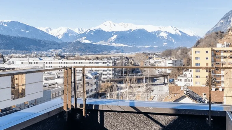 Geräumiger Balkon mit Teppichboden und atemberaubendem Blick auf die schneebedeckten Berge und die Stadt.