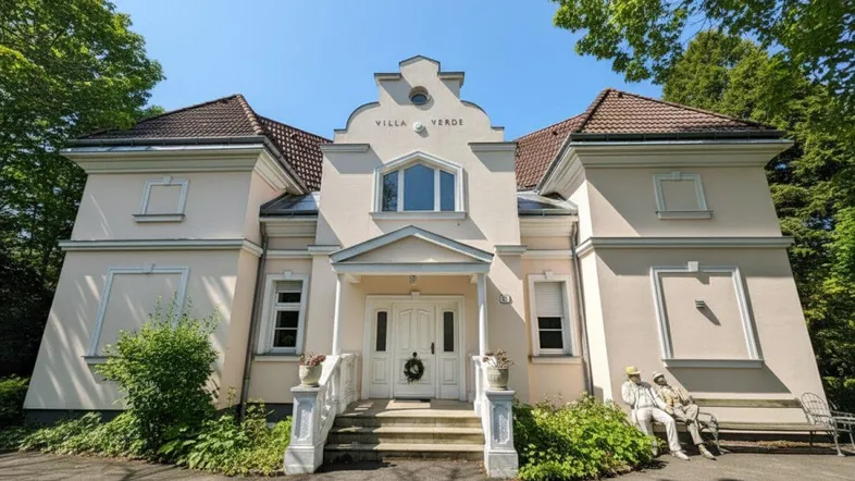 Elegante Villa mit klassischer Architektur, hellem Anstrich und gepflegtem Vorgarten.