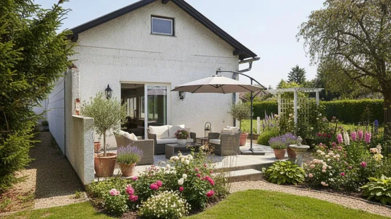 Einladende Terrasse mit Gartenmöbeln, Sonnenschirm und blühenden Beeten im Garten.