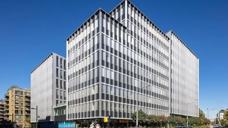 Modernes Bürogebäude mit markanter Glas- und Metallfassade unter blauem Himmel in urbaner Umgebung.