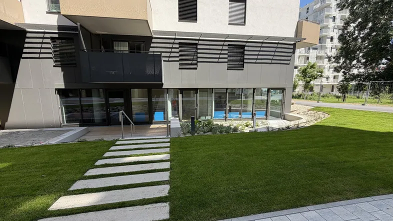Moderne Architektur eines Neubaus mit großen Glasfronten im Erdgeschoss und gepflegter Grünfläche.
