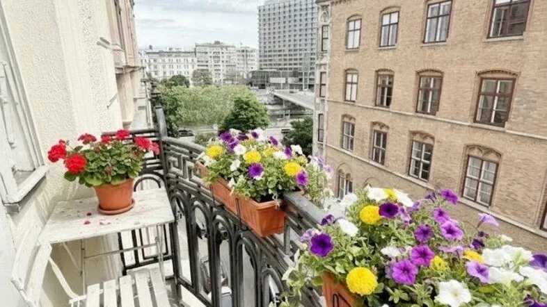 Heller Balkon mit schmiedeeisernem Geländer, bunten Blumenkästen und Stadtblick.